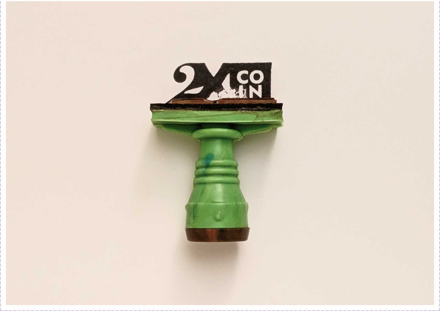 Green rubber stamp with the 2XCOIN mark on cream paper